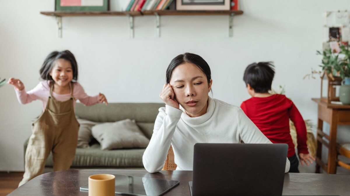 A tired mom working on a laptop while her children play - coping with mom stress