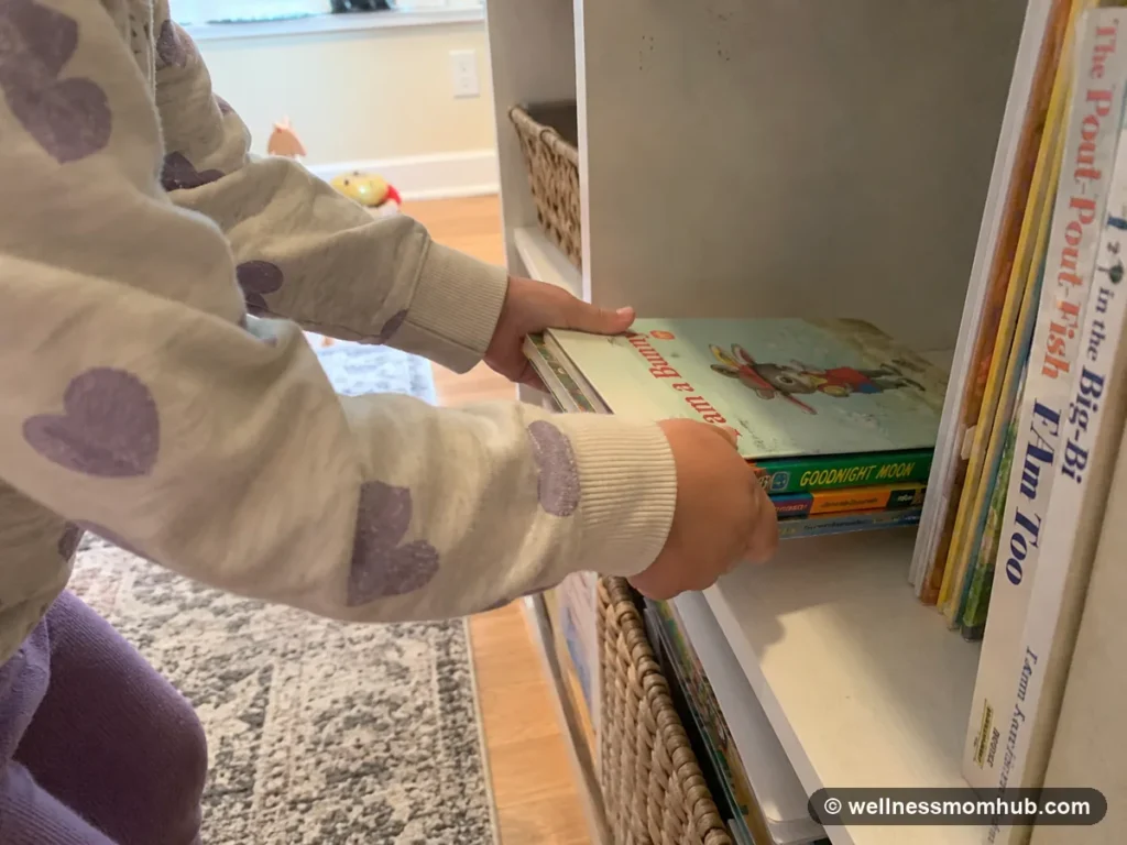 Young child placing books onto a low shelf as one of the chores for 3 year olds