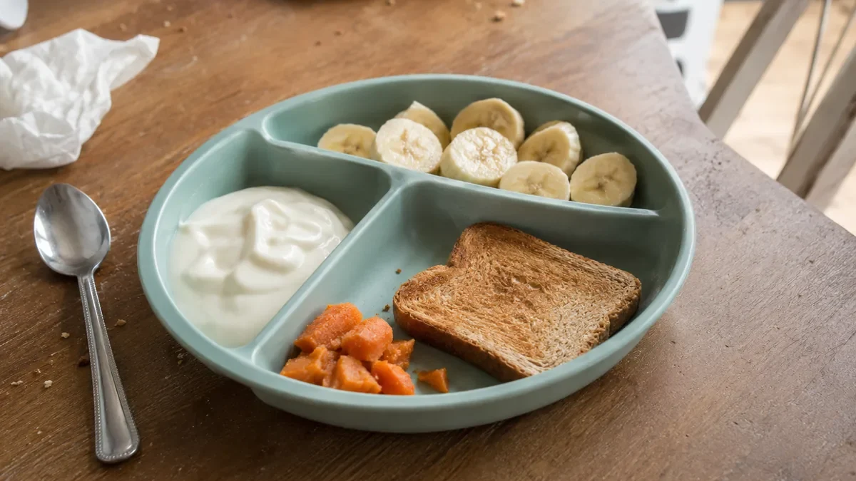 Divided toddler plate with banana, plain yogurt, toast, and soft cooked sweet potato